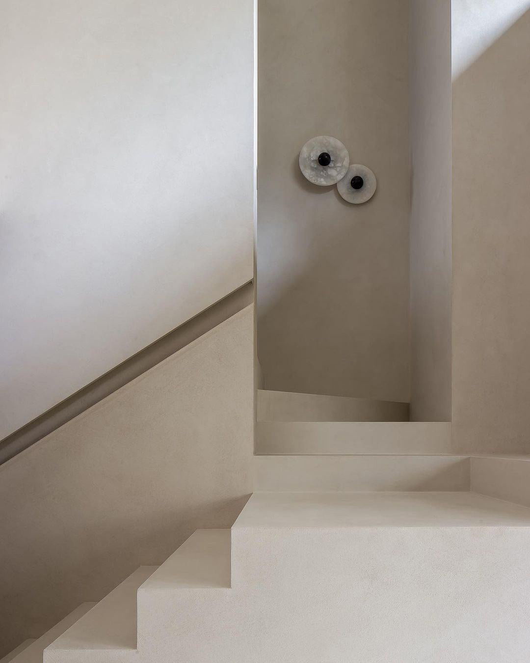 Two Clérachic round alabaster sconces on a stair wall in soft daylight.