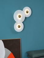 Three Clérachic round alabaster sconces lit on a deep teal wall above stacked artwork.
