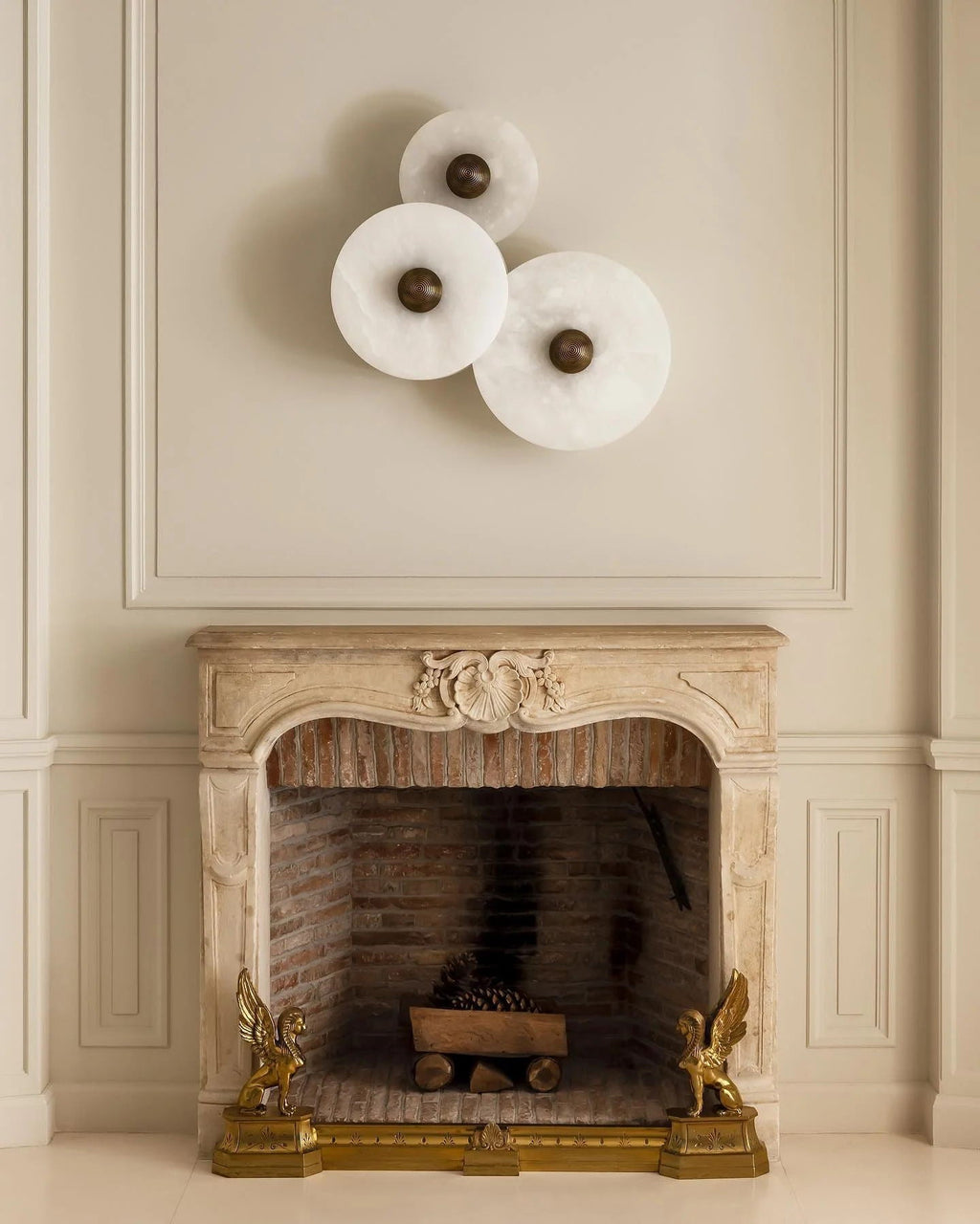 Three Clérachic round alabaster sconces above a carved stone fireplace in a panelled room.