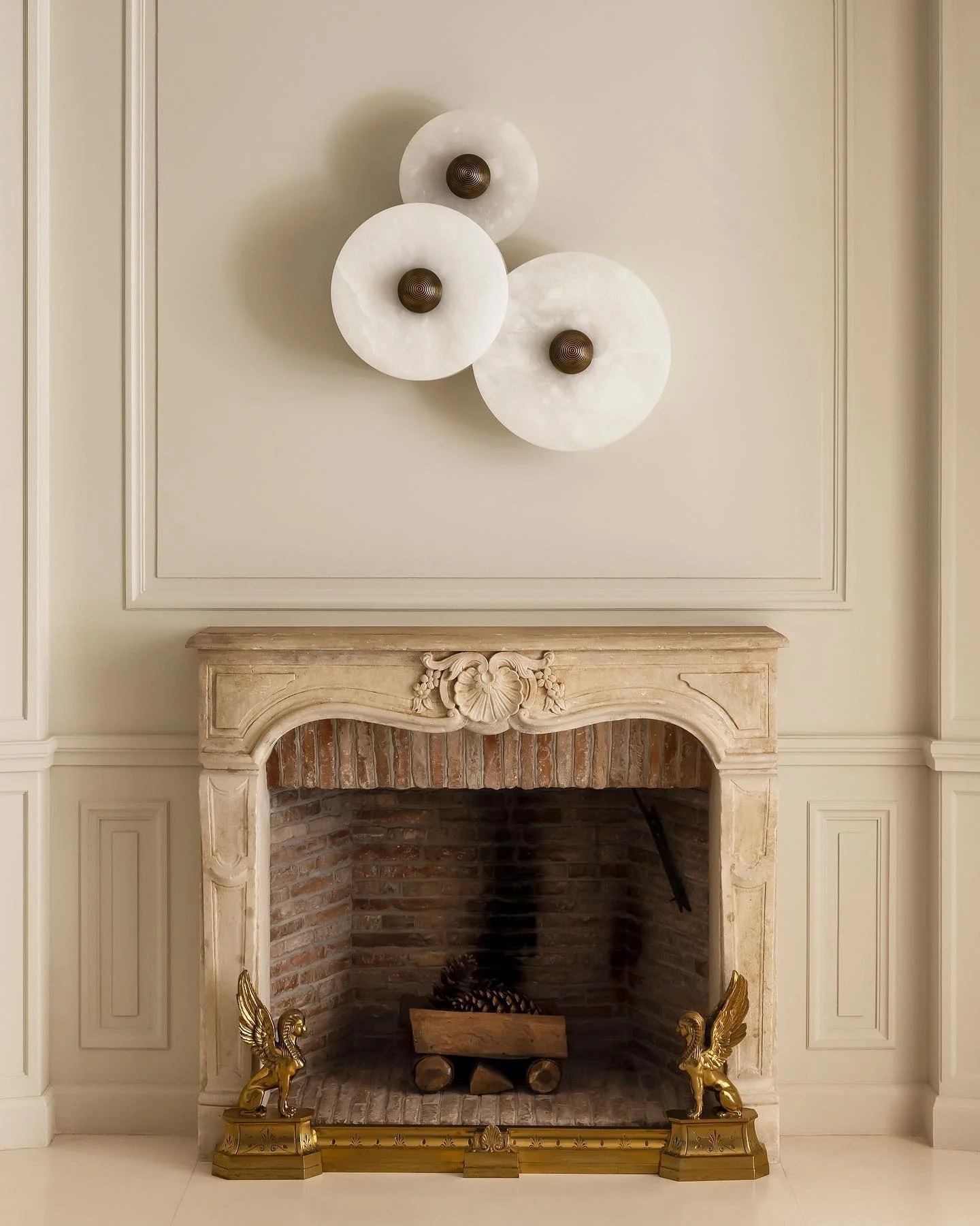 Three Clérachic round alabaster sconces above a carved stone fireplace in a panelled room.