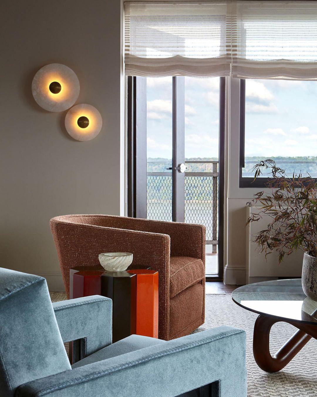 Two Clérachic round alabaster sconces lit in a living room with a balcony and sea view.