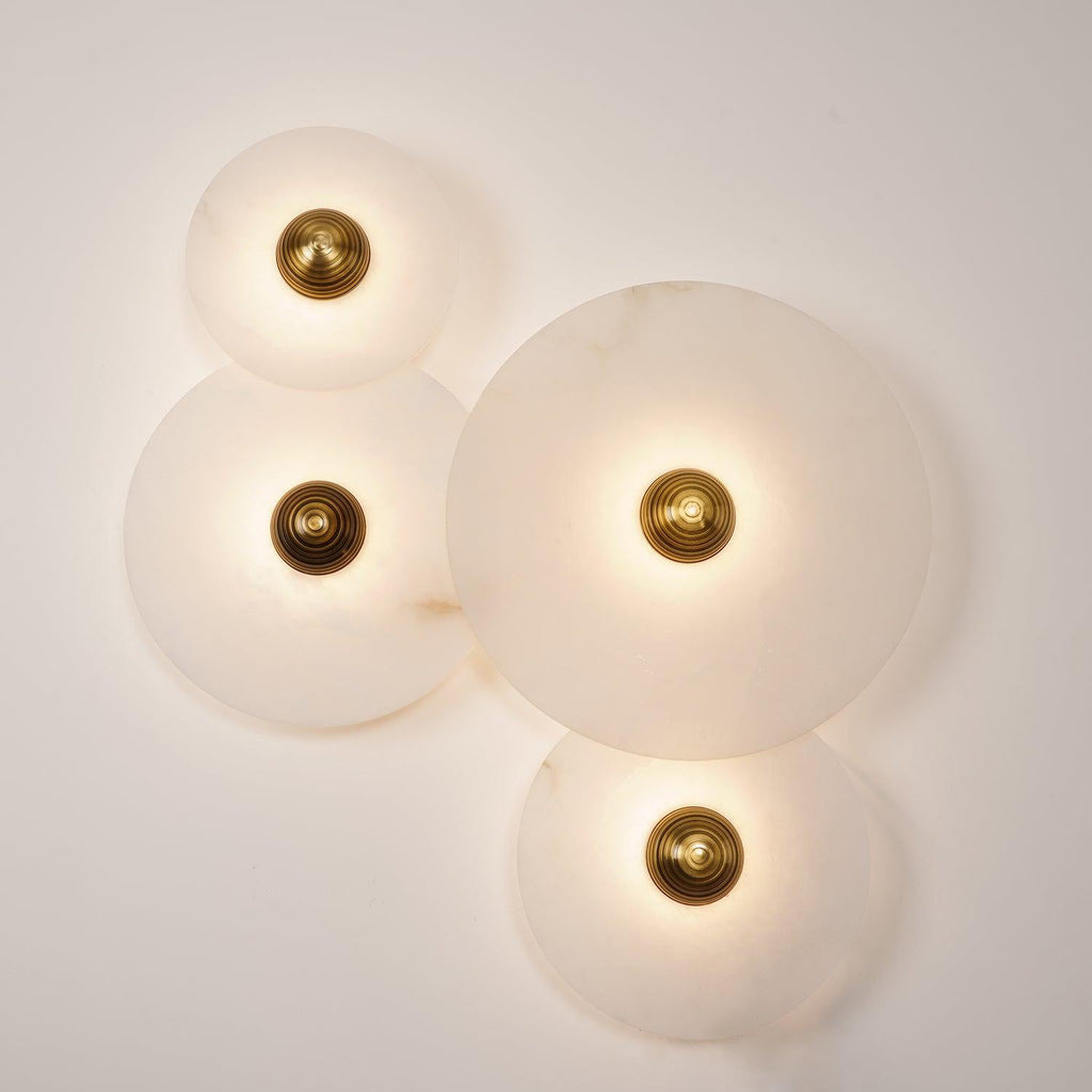 Four Clérachic round alabaster sconces lit warm, discs overlapping across the wall.