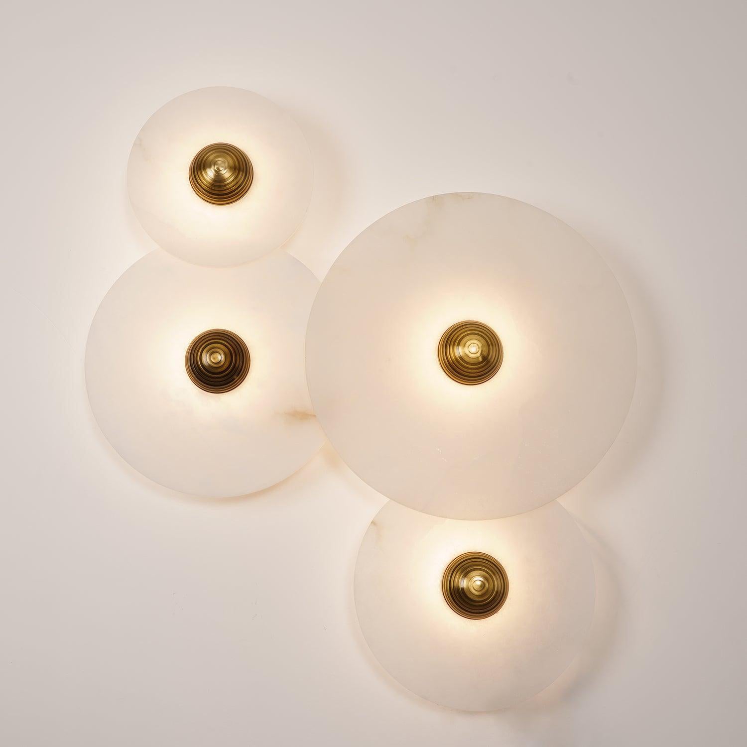Four Clérachic round alabaster sconces lit warm, discs overlapping across the wall.