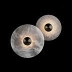 Two Clérachic round alabaster sconces on black, one lit and one dark, showing the veining.