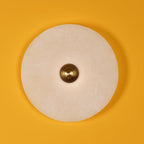 A single Clérachic round alabaster sconce on a saffron wall, fluted brass boss at its centre.