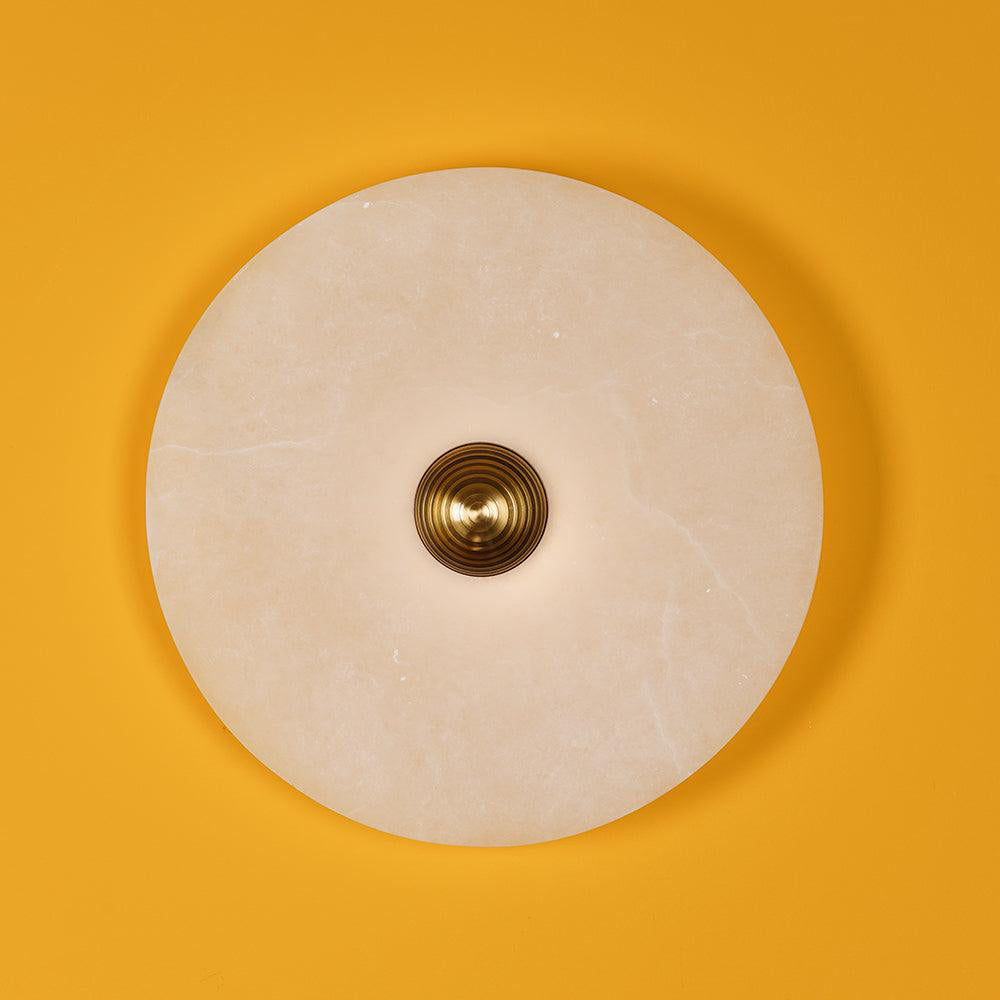 A single Clérachic round alabaster sconce on a saffron wall, fluted brass boss at its centre.