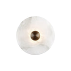 Clérachic round alabaster sconce lit on white, soft halo spreading out from the brass boss.