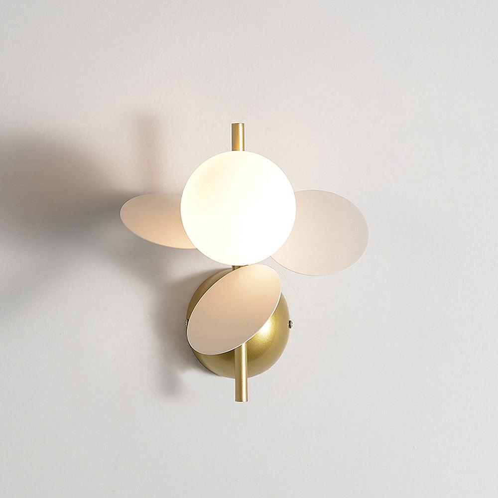 White version of this Clérachic wall light, a lit glass globe with cream discs and a brass dome mount on a light grey wall.