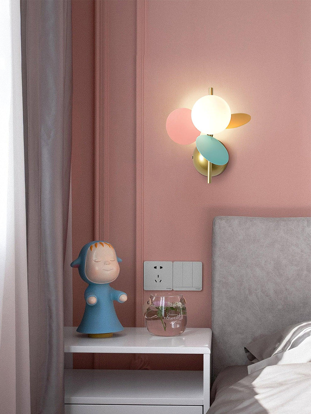 Pink, mint and orange Clérachic wall light against a dusty-pink wall, over a bedside table with a small blue figurine.