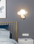 White-disc Clérachic wall light beside a gold-framed bed on a grey wall, with a white chest of drawers underneath.