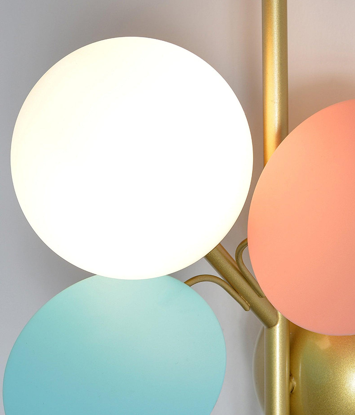 Close view of the frosted glass globe, a pink disc and a mint disc on the brass stem of this Clérachic wall light.