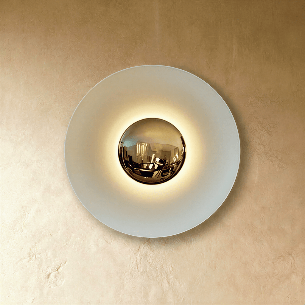 Clérachic round wall lamp in studio light: a pale white disc with a mirrored brass dome and a soft glow around it.