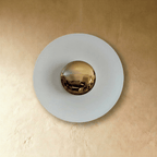 Clérachic round wall lamp switched off in studio light, showing the plain white disc and its polished brass mirror dome.