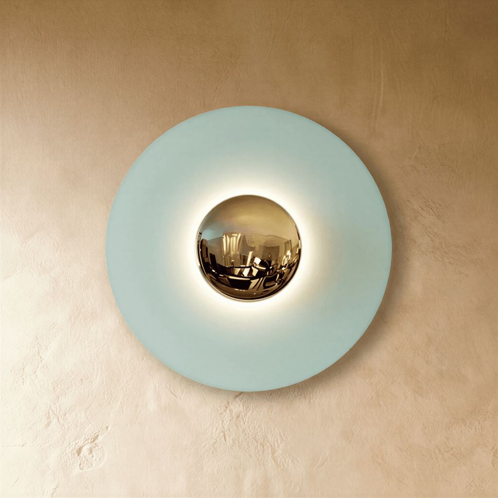 Clérachic round wall lamp in studio light with a pale blue disc, a polished brass mirror dome and a warm halo behind it.