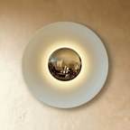 Clérachic larger round wall lamp in studio light: a white disc with a polished brass mirror dome and warm light behind.