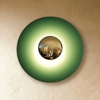 Clérachic larger round wall lamp in studio light with a green disc, a brass mirror dome and a bright glow at the centre.