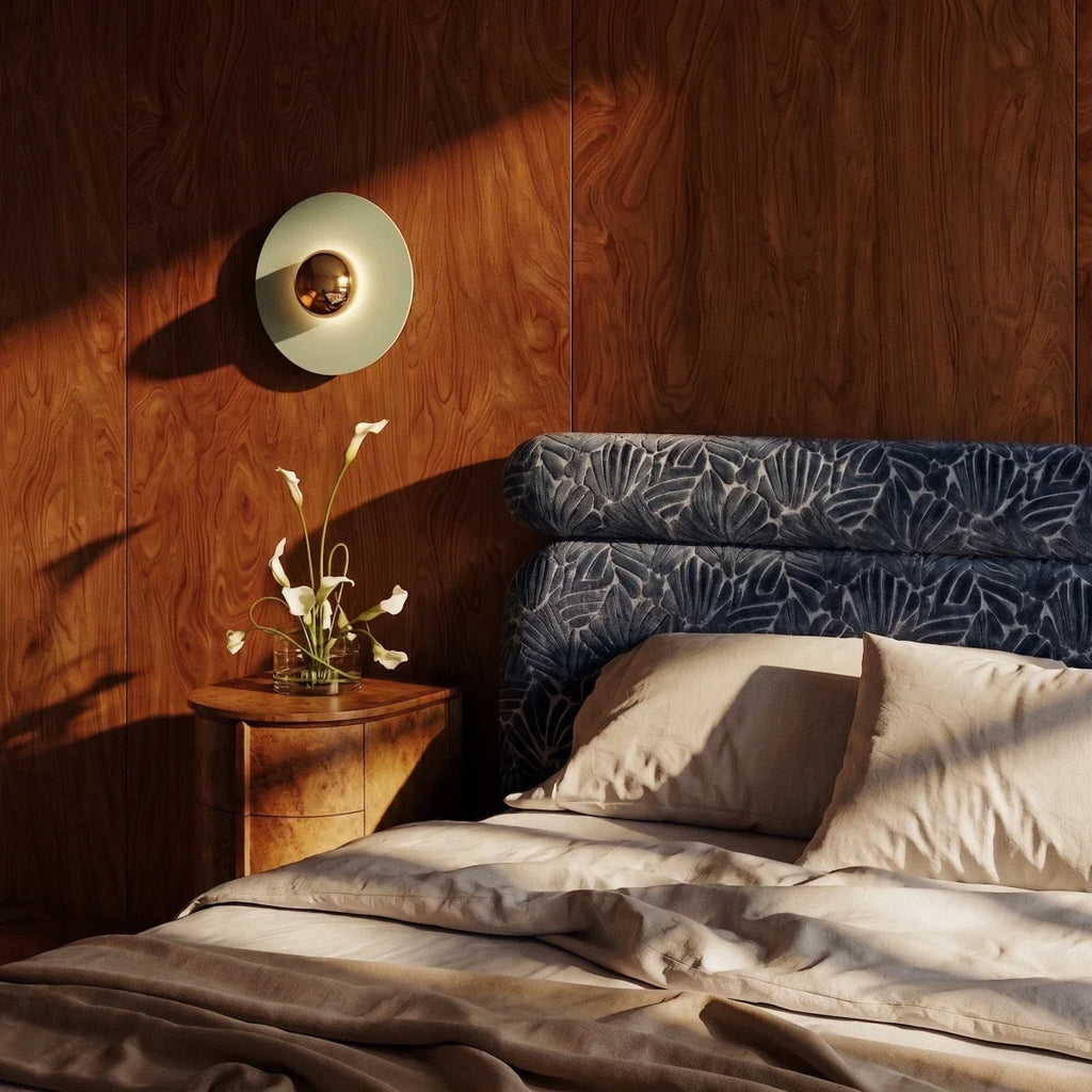 Clérachic round wall lamp with a pale green disc and brass dome on a walnut-panelled bedroom wall above a bedside table.