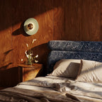 Clérachic round wall lamp with a pale green disc and brass dome on a walnut-panelled bedroom wall above a bedside table.