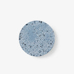 A Clérachic round wall light with a blue terrazzo face flecked in white and grey, on a plain white backdrop.