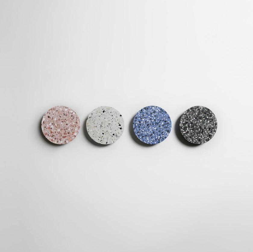 Four Clérachic round wall lights in pink, white, blue and black terrazzo hang in a row on a white wall.
