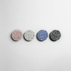 Four Clérachic round wall lights in pink, white, blue and black terrazzo hang in a row on a white wall.