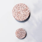 Two Clérachic round wall lights in pink terrazzo, one large and one small, mounted on a soft white wall.