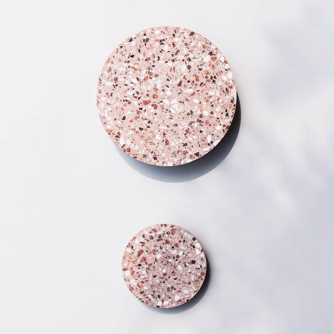Two Clérachic round wall lights in pink terrazzo, one large and one small, mounted on a soft white wall.