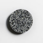 A Clérachic round wall light with a black terrazzo face and white and grey chips, casting a soft shadow on a pale wall.