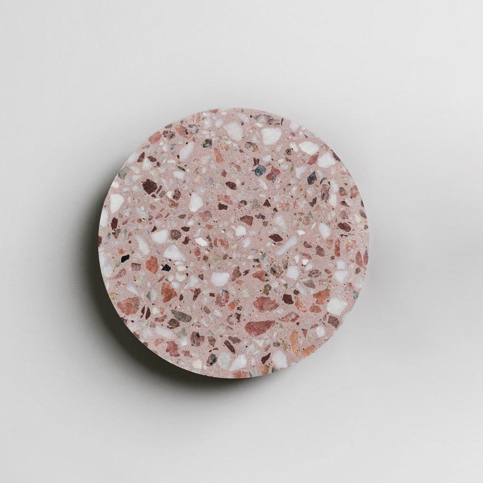 A Clérachic round wall light in pink terrazzo on a pale wall, with a soft shadow along its lower edge.