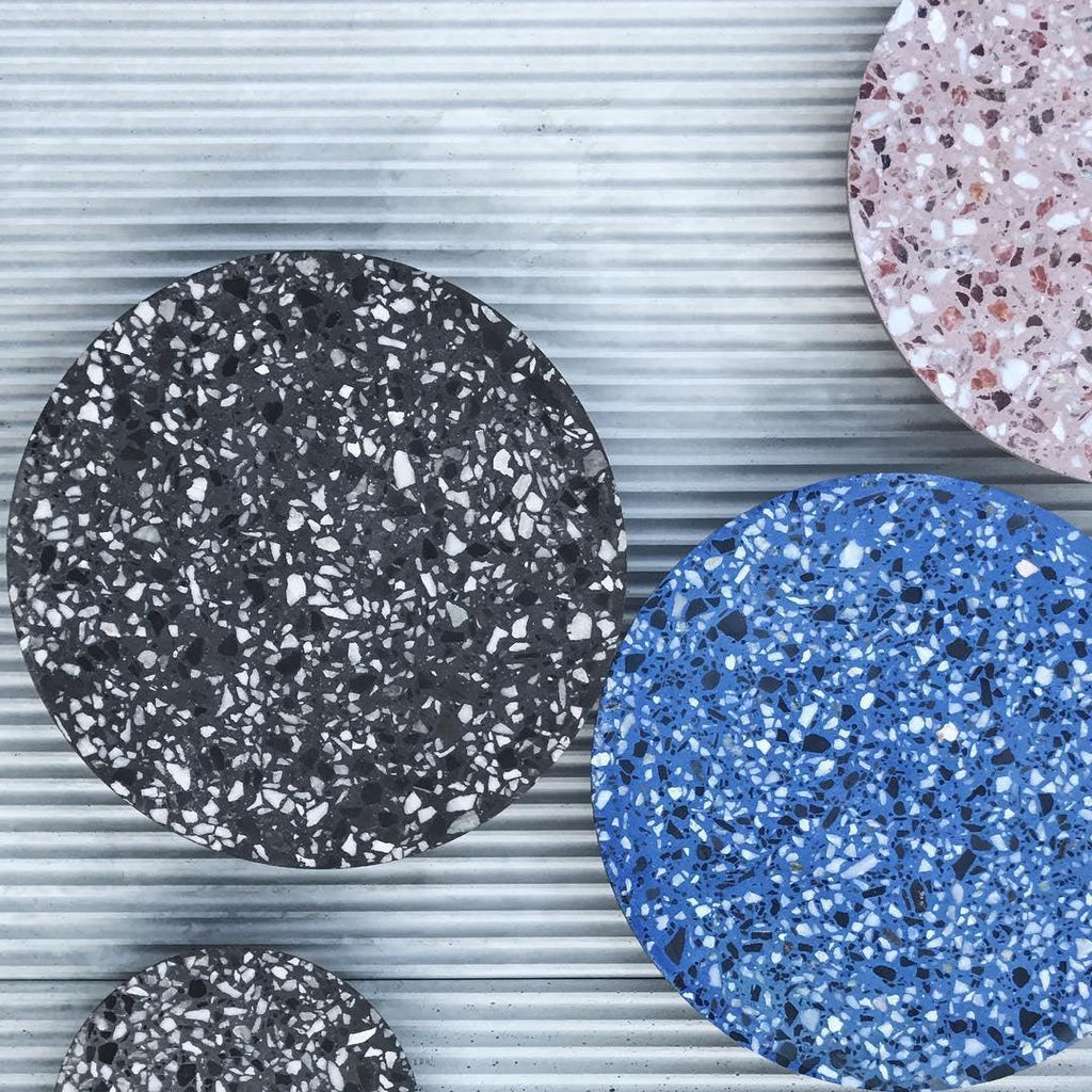 Close view of the black and blue terrazzo faces of these Clérachic round wall lights on a ribbed metal wall.