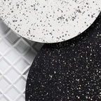 Close view of white and black terrazzo faces on two Clérachic round wall lights, set against a patterned white tile.