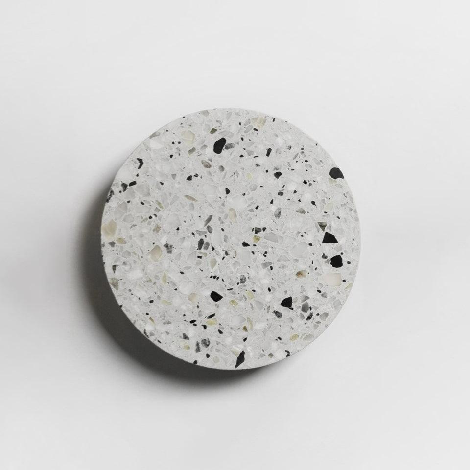 A Clérachic round wall light with a white terrazzo face flecked with black and grey, on a pale wall.