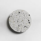 A Clérachic round wall light with a white terrazzo face flecked with black and grey, on a pale wall.