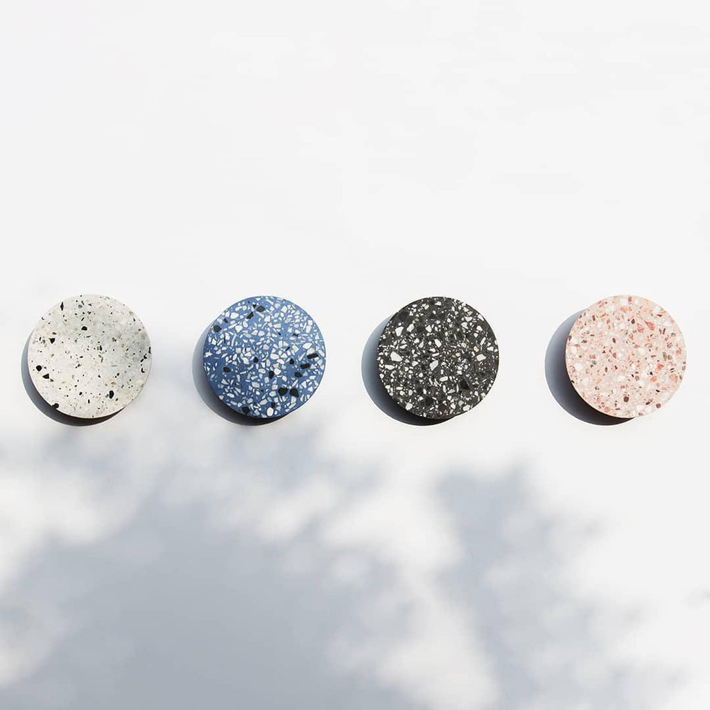 Four Clérachic round wall lights in white, blue, black and pink terrazzo, spaced in a row on a pale wall.