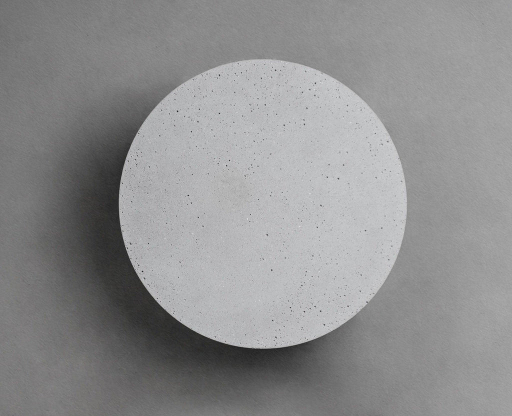 A Clérachic round wall light with a pale cement-grey face on a mid-grey wall, with a soft shadow at its edge.