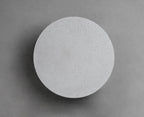 A Clérachic round wall light with a pale cement-grey face on a mid-grey wall, with a soft shadow at its edge.