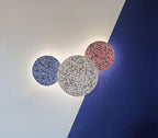 Three Clérachic round wall lights in blue, white and pink terrazzo glow on a wall split into white and deep blue.