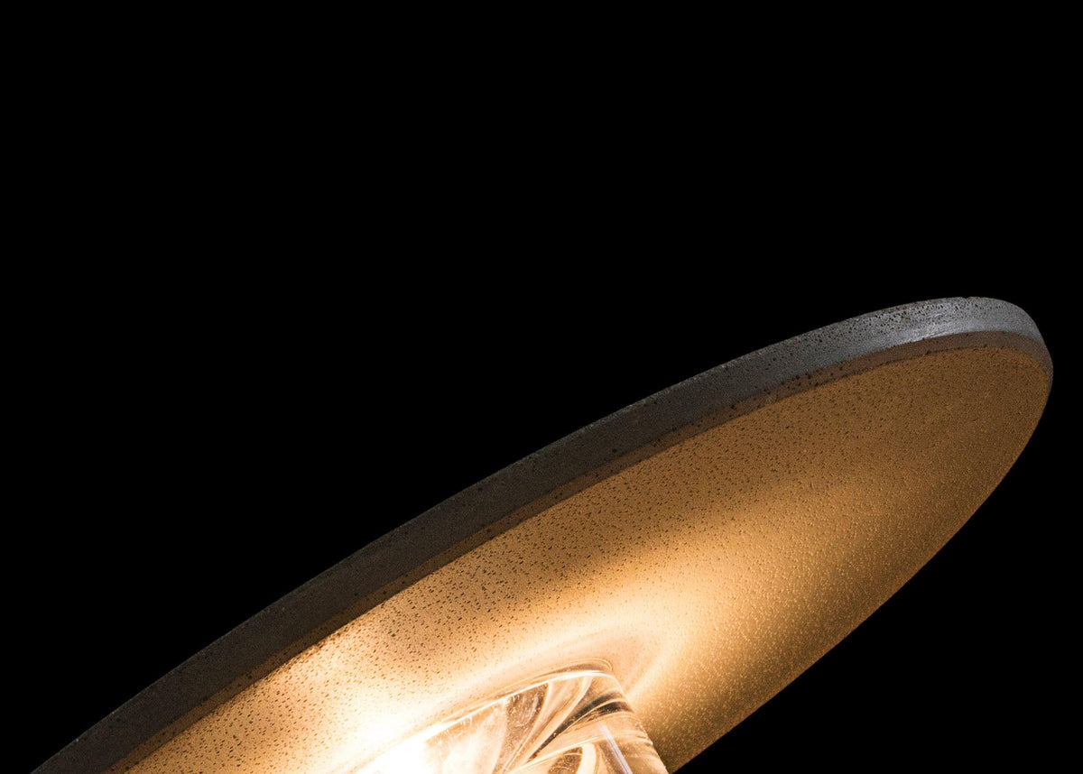 Close view from below of the underside of a Clérachic round wall light, with warm light glowing inside against black.
