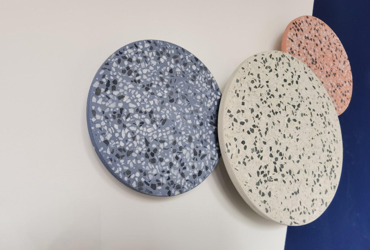 Blue, cream and pink terrazzo Clérachic round wall lights overlap on a white wall beside a deep blue panel.