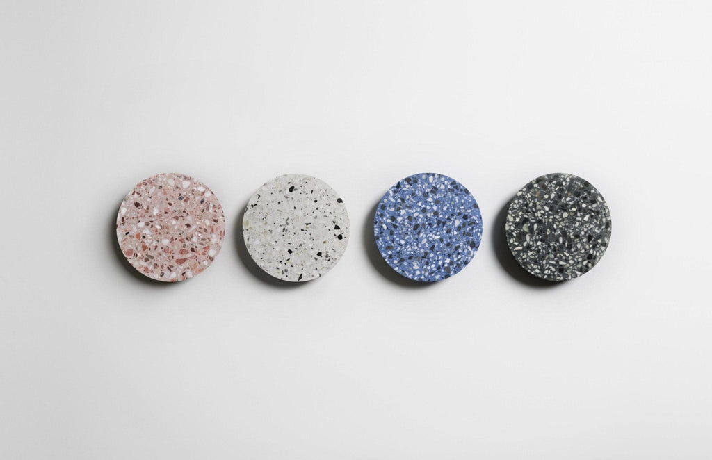 Four Clérachic round wall lights in pink, white, blue and black terrazzo lined up on a pale wall.