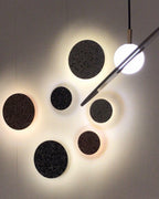 Six Clérachic round wall lights in dark terrazzo hang in a cluster, each with a warm halo, beside a globe pendant light.