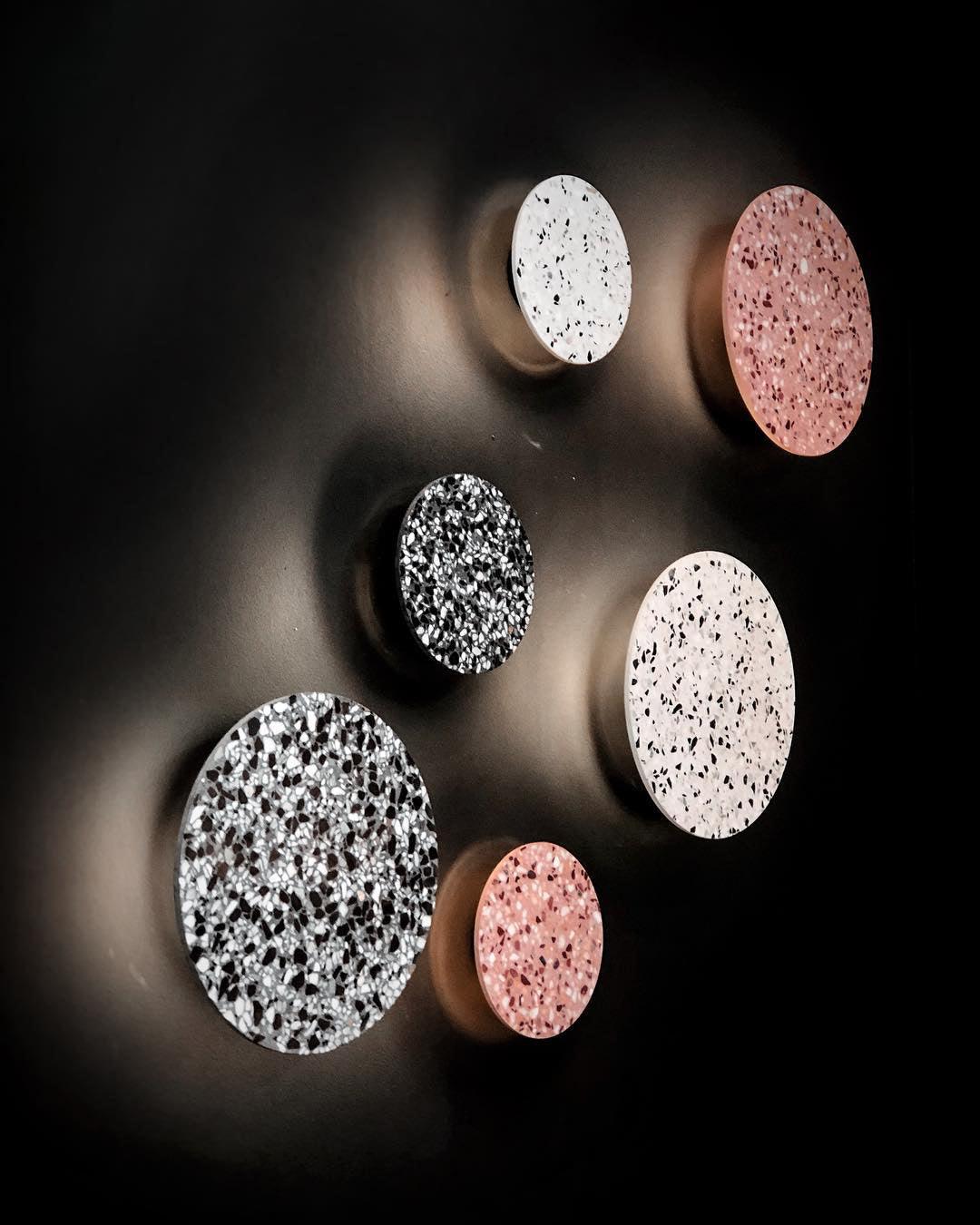 A cluster of white, black and pink terrazzo Clérachic round wall lights, lit warmly on a very dark wall.