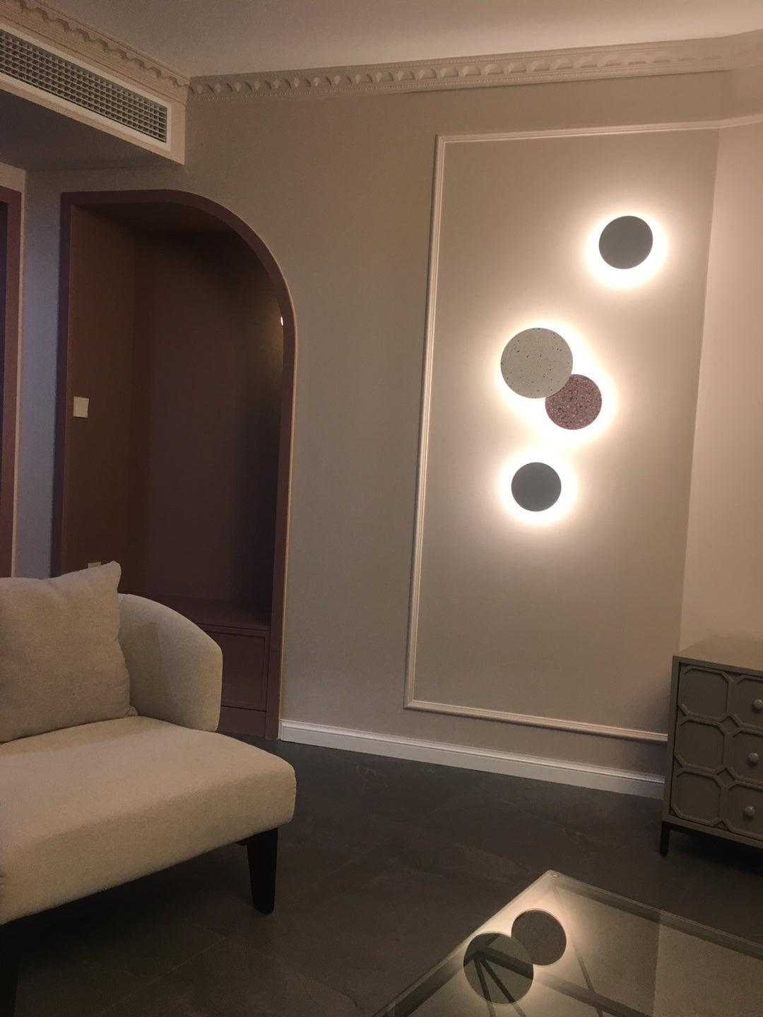 Three Clérachic round wall lights in grey and pink tones glow softly on a panelled wall beside an arched doorway.