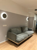 A Clérachic round wall light glows beside a second one in a lounge with a grey sofa and pale wood floor.