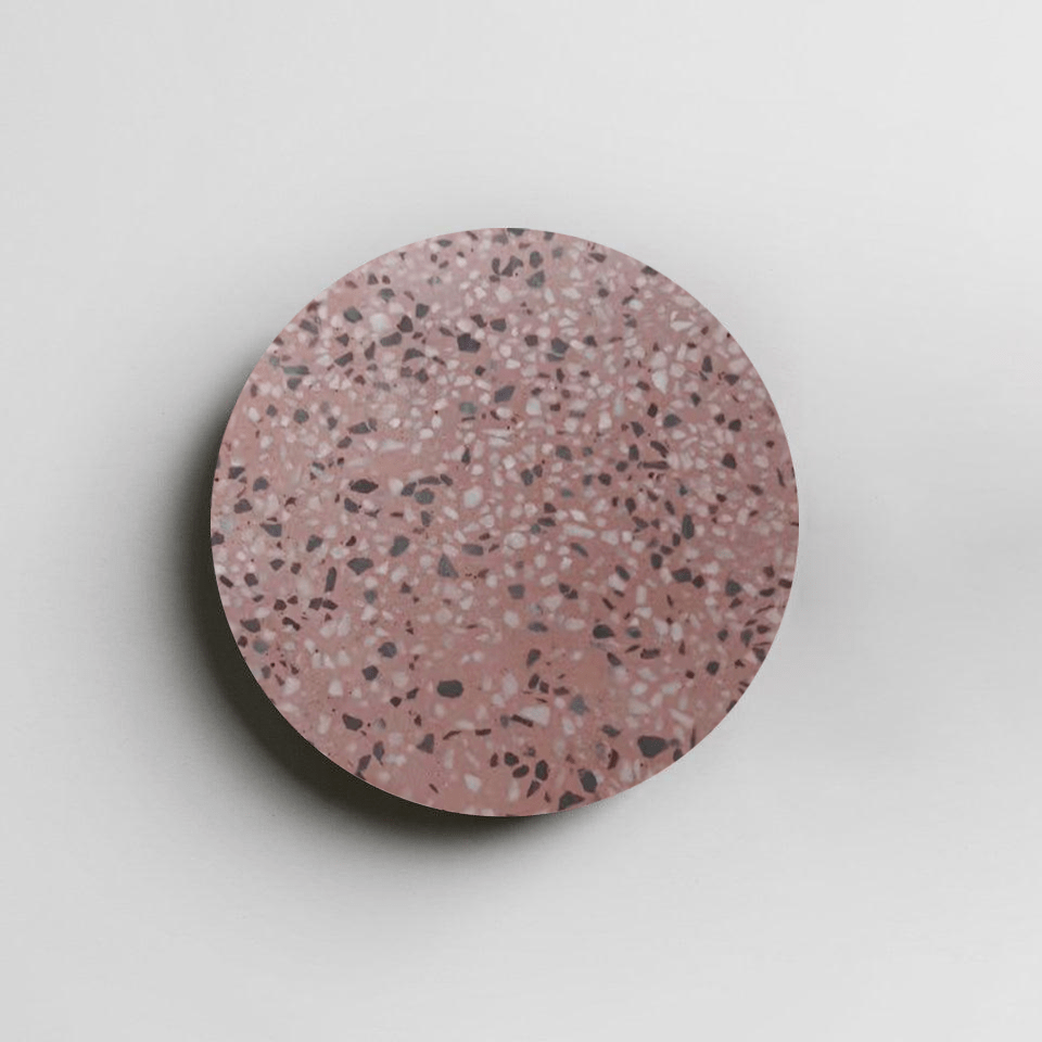 A Clérachic round wall light with a pink terrazzo face, flecked in grey and white, on a pale backdrop.