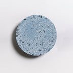 A Clérachic round wall light with a blue terrazzo face, shown close up with a soft shadow on a pale wall.
