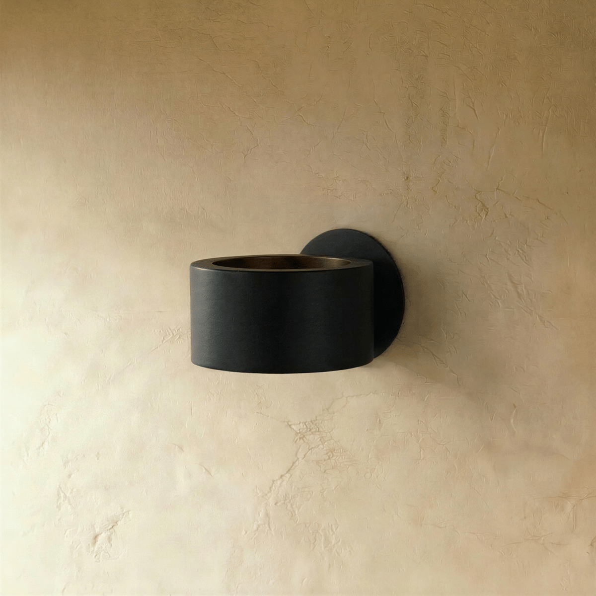 Clérachic round black metal wall lamp, switched off, with a bronze-toned inner rim and a round wall plate on limewashed plaster.