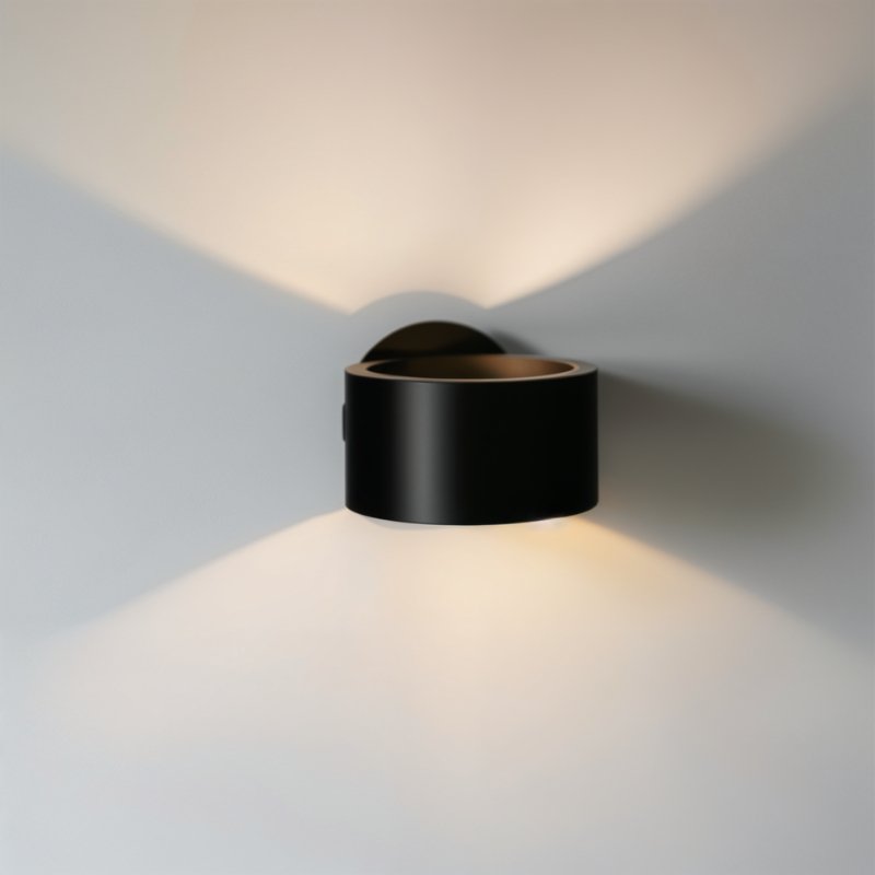 Clérachic round black wall lamp casting light up and down on a pale wall in two soft cones, with a bronze inner rim.