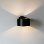 Clérachic round black wall lamp casting light up and down on a pale wall in two soft cones, with a bronze inner rim.