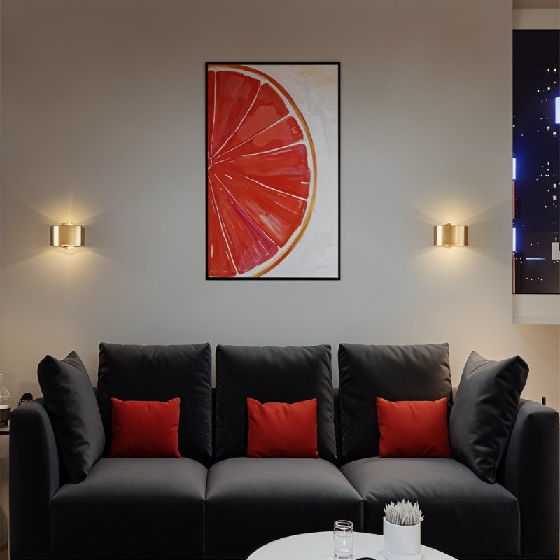 Clérachic two gold drum wall lamps flanking a framed grapefruit print above a black sofa with red cushions.